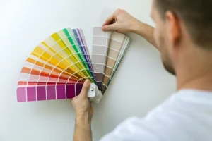 A person holding up paint swatches to a wall in a room of their Springfield, IL home to determine the psychological aspects of each color.